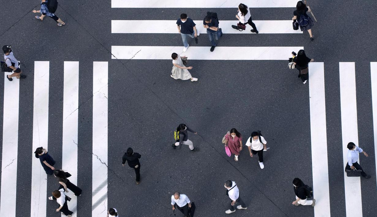 Warga yang mengenakan masker untuk membantu mengekang penyebaran COVID-19 berjalan di sepanjang penyeberangan pejalan kaki di Tokyo, Jepang, Selasa (27/7/2021). Tokyo melaporkan jumlah kasus harian COVID-19 tertinggi beberapa hari setelah Olimpiade dimulai. (AP Photo/Eugene Hoshiko)