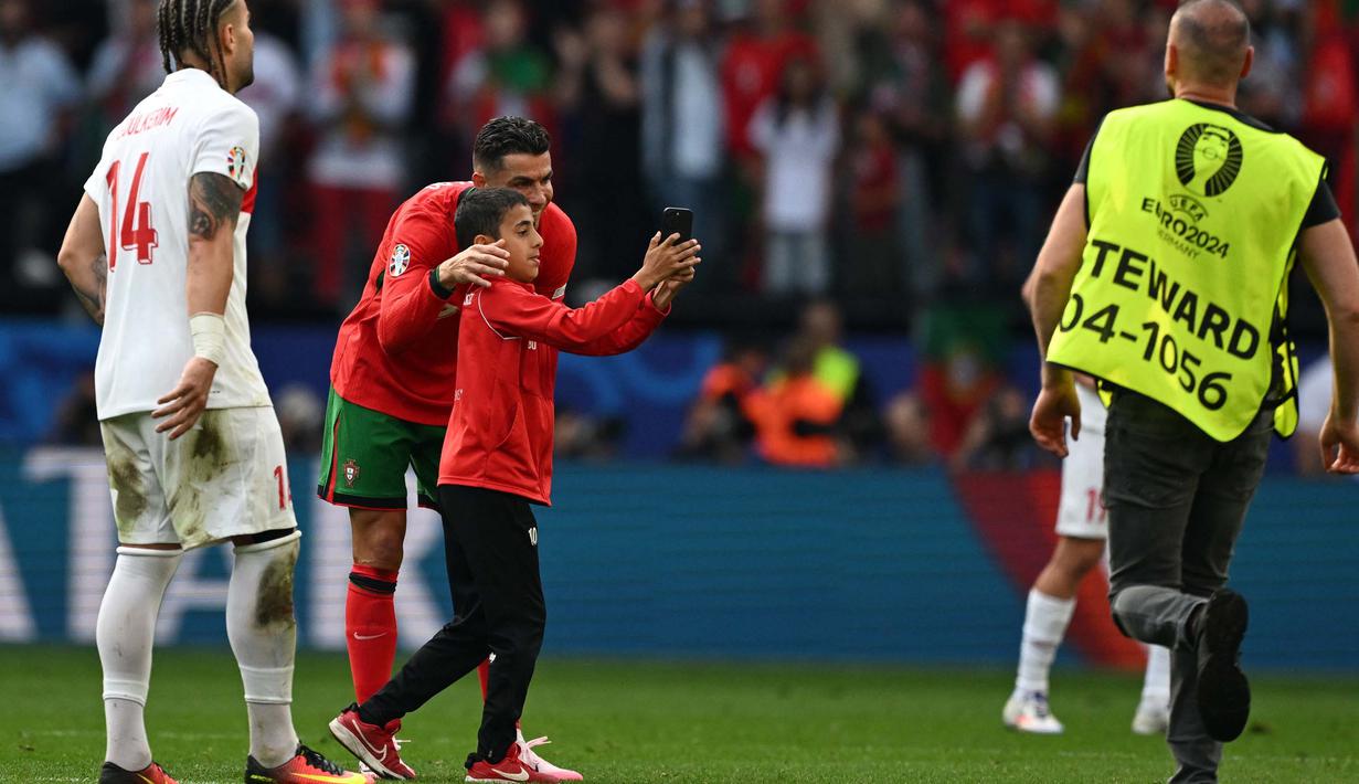 Penyerang Portugal, Cristiano Ronaldo berpose bersama seorang penyerbu lapangan muda selama pertandingan sepak bola Euro 2024 Grup F antara Turki dan Portugal di BVB Stadion, Dortmund pada 22 Juni 2024. (PATRICIA DE MELO MOREIRA/AFP)