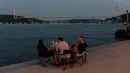 Orang-orang menikmati malam di sebelah pantai Bosphorus ketika jembatan Fatih Sultan Mehmet terlihat di Istanbul (6/7/2020). Jembatan Fatih Sultan Mehmet, yang dikenal dengan sebutan Jembatan Bosporus Kedua, adalah sebuah jembatan di Istanbul, Turki yang melintasi selat Bosporus. (AFP/Ozan Kose)