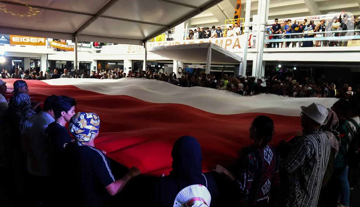 Pengunjung pameran produk berkegiatan di alam bebas atau Indofest 2023 membentangkan bendera Merah Putih di pelataran Istora Gelora Bung Karno, Jakarta, Kamis (1/6/2023). (Liputan6.com/Herman Zakharia)