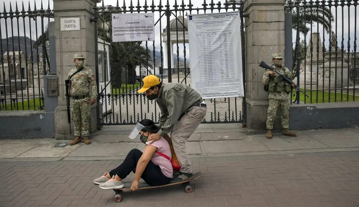 Sepasang kekasih bermain skate saat tentara berjaga di luar Pemakaman Maestro Presbitero, Lima, Peru, Minggu (1/11/2020). Untuk membantu mencegah penyebaran COVID-19, pihak berwenang menutup semua pemakaman secara nasional selama perayaan Day of the Dead. (AP Photo/Rodrigo Abd)