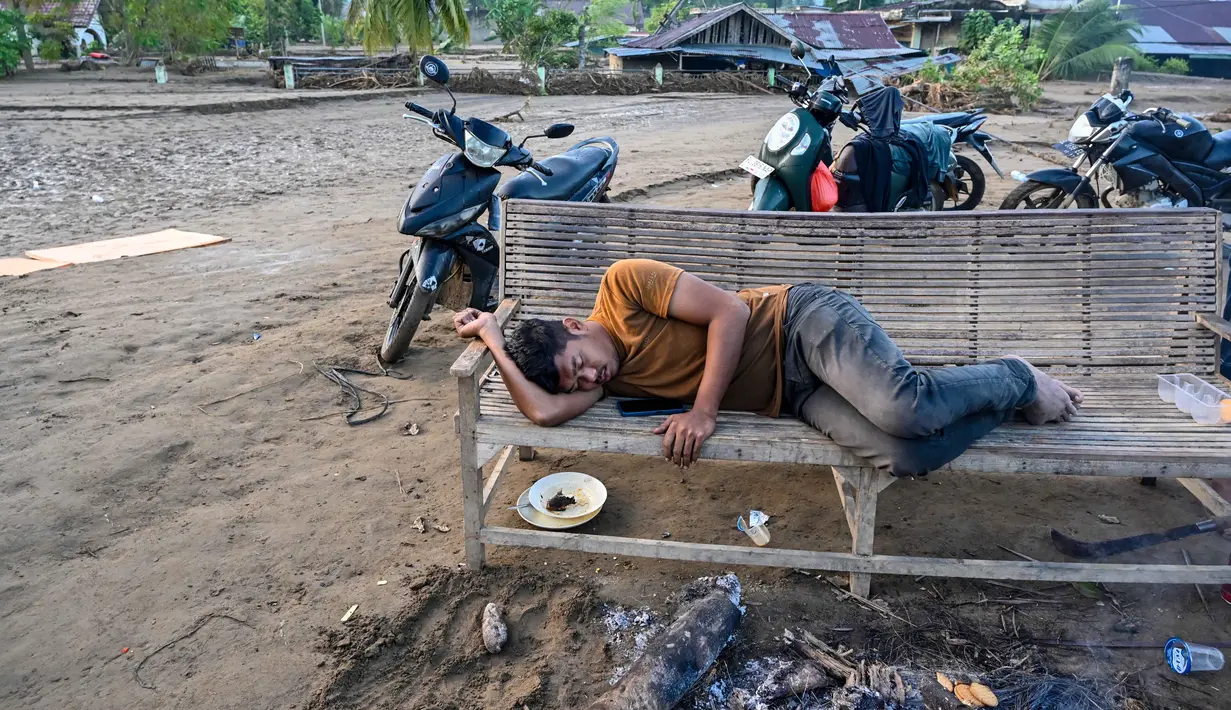 Seorang warga desa yang terdampak banjir tidur di bangku setelah banjir bandang melanda Meureudu, Kabupaten Pidie Jaya, Provinsi Aceh, pada 30 November 2025. Berdasarkan data dari Badan Penanggulangan Bencana Daerah (BPBD) Kabupaten Pidie Jaya, pada Jumat (28/11/2025), jumlah warga terdampak bencana hidrometerologi mencapai 90.000 jiwa dan yang mengungsi sekitar 12.000 jiwa. (CHAIDEER MAHYUDDIN/AFP)