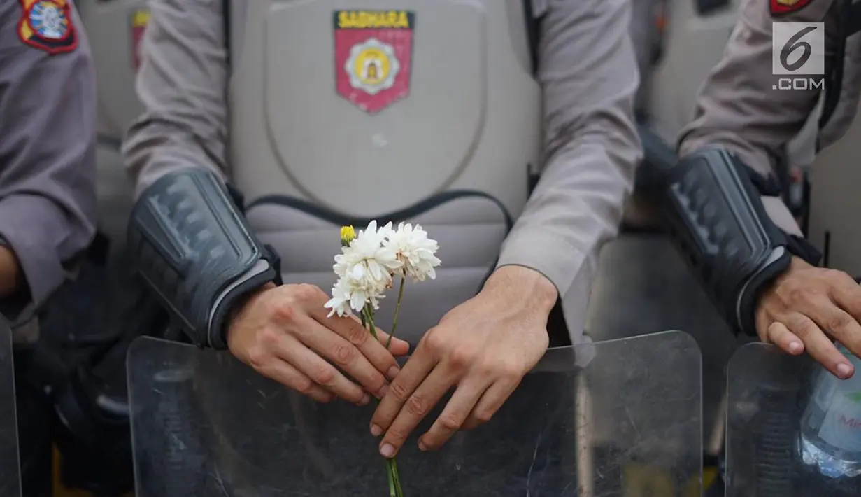 Personel polisi memegang bunga saat mengamankan aksi unjuk rasa Badan Eksekutif Mahasiswa Seluruh Indonesia (BEM SI) di sekitar DPR RI, Jakarta, Selasa (1/10/2019). Selain berorasi secara damai, mahasiswa membagikan bunga untuk para polisi yang mengawal aksi mereka. (Liputan6.com/Immanuel Antonius)