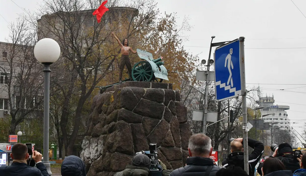 Sejumlah wartawan saat meliput seorang aktivis wanita gerakan hak perempuan Femen di tiang monumen Soviet di pusat kota Kiev, Ukraina (7/11). ). Aktivis tersebut menggelar aksi memperingati 100 tahun Revolusi Bolshevik. (AFP Photo/Genya Savilov)