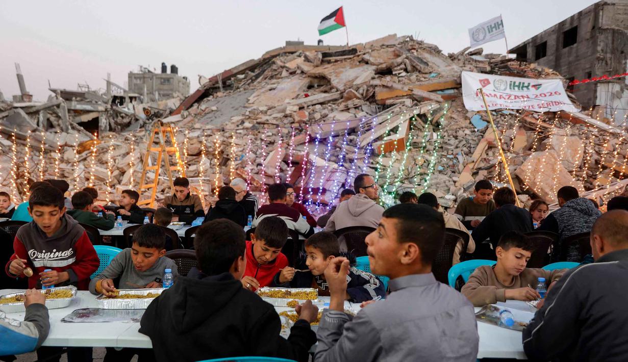 Warga Palestina berkumpul untuk berbuka puasa bersama yang diselenggarakan oleh Yayasan IHH Turki, di tengah reruntuhan bangunan yang hancur di Kota Gaza pada Rabu 18 Februari 2026. Puluhan hingga ratusan warga Palestina di Gaza duduk bersama untuk berbuka puasa bersama di antara puing-puing bangunan yang hancur. (Omar AL-QATTAA/AFP)
