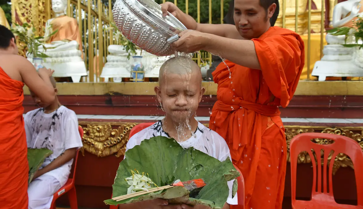 Biksu mengguyur kepala salah satu anak, yang diselamatkan dari gua di Thailand, pada upacara pentahbisan di Kuil Wat Phra That Doi Wao, Chiang Rai, Selasa (24/7). Sebanyak 11 remaja menjalani ritual menjadi biksu. (Panumas Sanguanwong/THAI NEWS PIX/AFP)