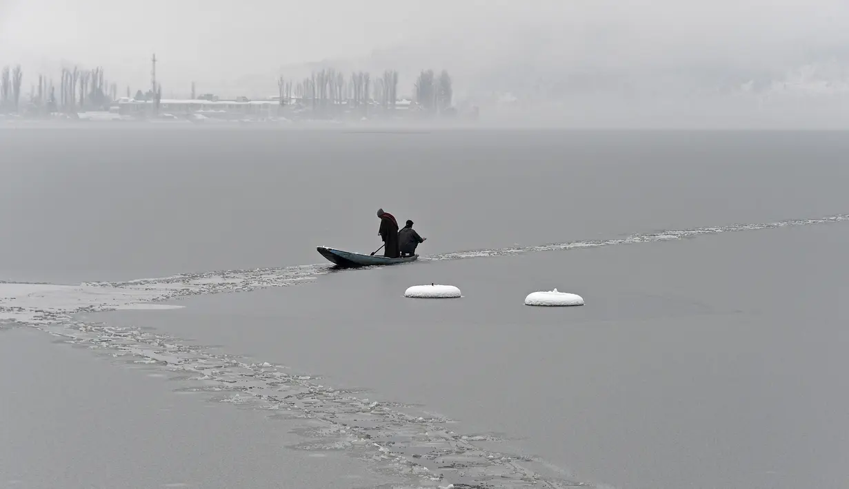 Seorang pria mengendarai perahu di dekat bagian beku danau Dal setelah hujan salju lebat di Srinagar 16/1/2020). Temperatur telah turun beberapa tingkat di bawah titik beku. (AFP Photo/Tauseef Mustafa)