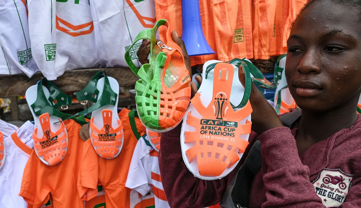 Seorang pedagang menunjukkan dagangannya berupa sendal bernuansa Piala Afrika 2023 di salah satu pasar Abidjan, pusat kota Pantai Gading. (AFP/Issouf Sanogo)