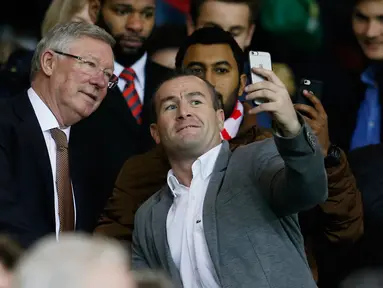 Mantan manajer Manchester United Sir Alex Ferguson berselfie dengan fans saat menyaksikan pertandingan antara Manchester United dengan Chelsea di Stadion Old Trafford, Inggris (28/12). MU bermain imbang dengan Chelsea dengan skor 0-0. (Reuters/Phil Noble)