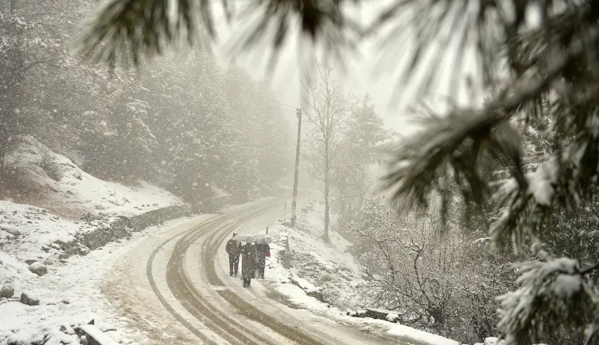 Pejalan kaki melewati sepanjang jalan yang tertutup salju di Gulmarg, sekitar 55 km sebelah utara Srinagar, Kashmir, Selasa (3/1). Gelombang dingin yang melanda Kashmir kian parah hingga mencapai suhu di bawah nol derajat celcius. (Tauseef Mustafa/AFP)