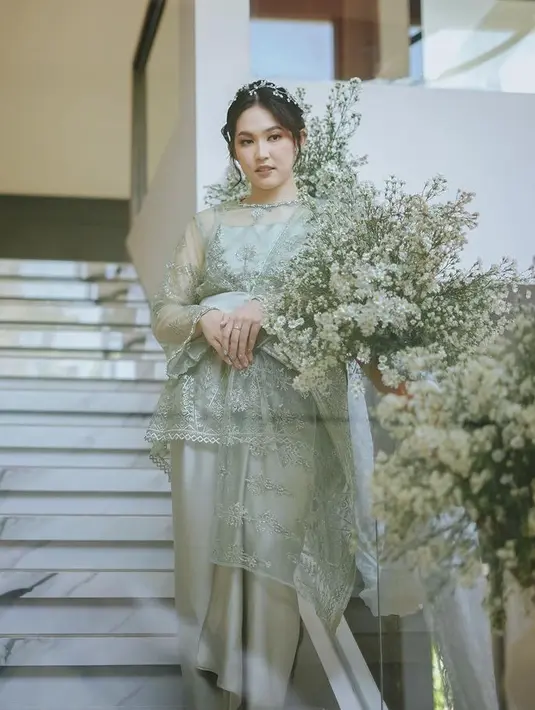 Ribka memilih tampil busana dengan warna sage, mulai dari atasan tunik berbordir lengan panjang semi transparan, dipadukan inner spaghetti strap, obi polos, dan kain lilit polos sebagai bawahannya. [@rvsdphoto]