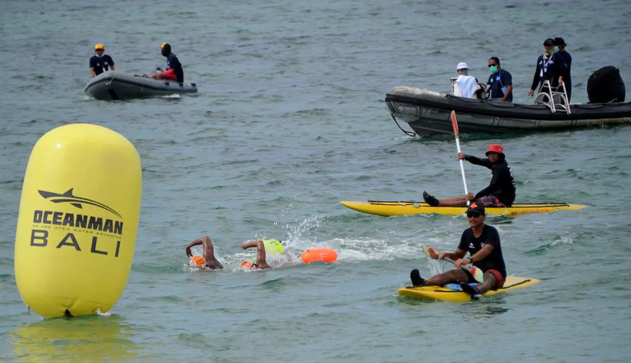 Para peserta bertanding sambil ditonton oleh kru pendukung dalam kompetisi renang Oceanman Bali 2021 di sebuah pantai di Sanur, Denpasar, Bali, Sabtu (18/9/2021). Oceanman Bali 2021 akhirnya sukses digelar setelah beberapa kali ditunda. (SONY TUMBELAKA/AFP)