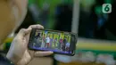 Seorang pria menggunakan ponselnya menyaksikan tontonan lenong Betawi yang disiarkan secara virtual di Jakarta, Selasa (8/12/2020). Kegiatan tersebut bertujuan untuk memberdayakan kembali seniman Betawi yang sempat terhenti di masa pandemi COVID-19. (Liputan6.com/Faizal Fanani)