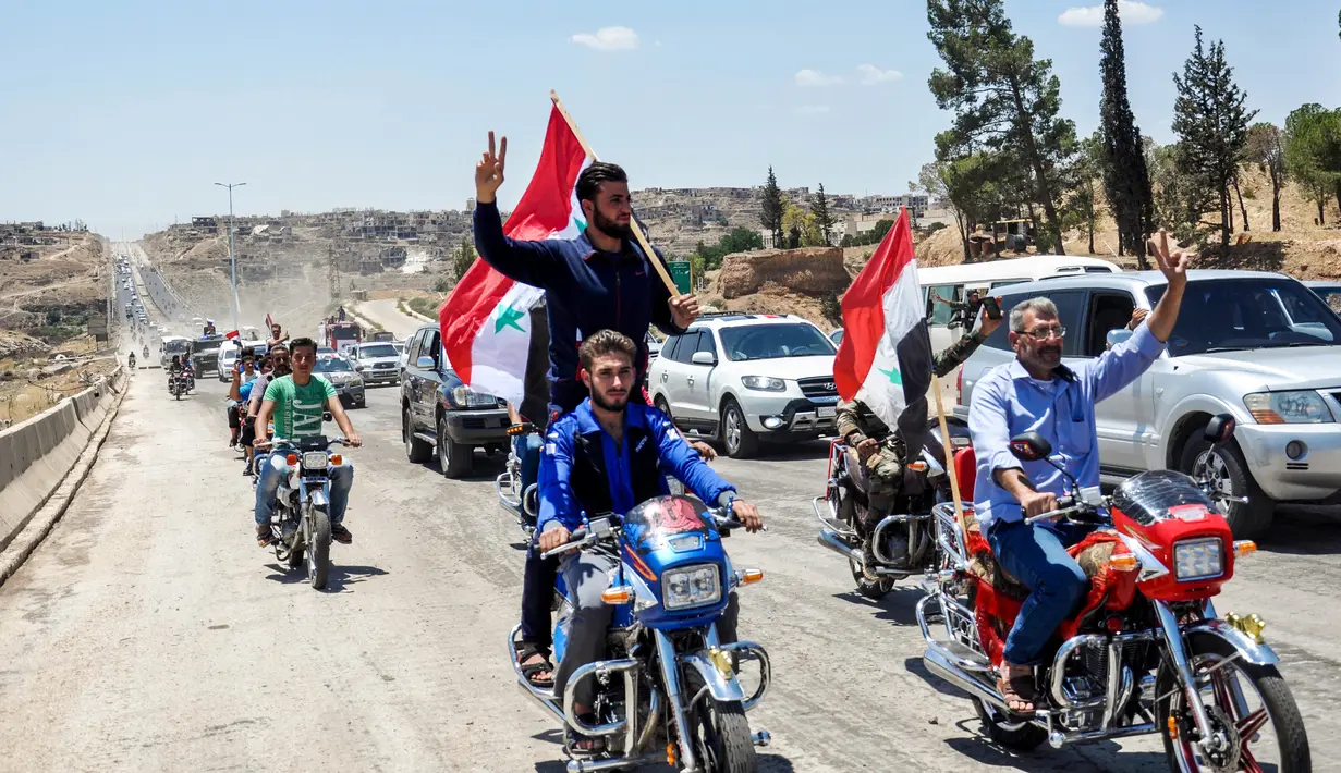 Pengendara motor mengibarkan bendera Suriah saat melintasi jalan raya utama antara Homs dan Hama yang dibuka kembali, Rabu (6/6). Pemerintah Suriah membuka kembali jalan raya Homs-Hama setelah ditutup selama hampir tujuh tahun. (AFP/STRINGER)