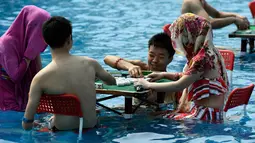 Pengunjung bermain mahjong di dalam kolam renang di wilayah Chongqing, Tiongkok, Rabu (2/8). Pemerintah setempat telah mengeluarkan peringatan merah terkait cuaca panas dengan suhu di beberapa daerah hampir mencapai 40 derajat celcius. (STR / AFP)
