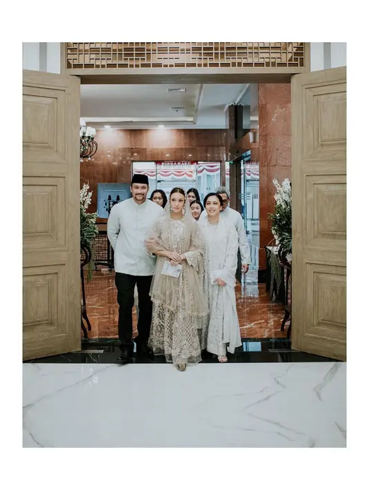 Abayanya hadir dengan kombinasi bahan lace-satin dan memiliki aksen plisket di bagian bawah.  Detail lengan bell dan kerah leher berbentuk “U” membuat penampilan Nabila kian anggun.  Penampilan Nabila disempurnakan dengan kerudung coklat transparan berdetail manik-manik emas di bagian tepiannya. [@nocture_co].