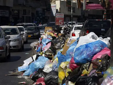 Kendaraan melintas di samping tumpukan sampah di sepanjang sisi jalan di Tripoli, ibukota Libya (30/9/2019). Berton-ton sampah berserakan dari tempat sampah dan menumpuk di pinggir jalan. (AFP Photo/Mahmud Turkia)
