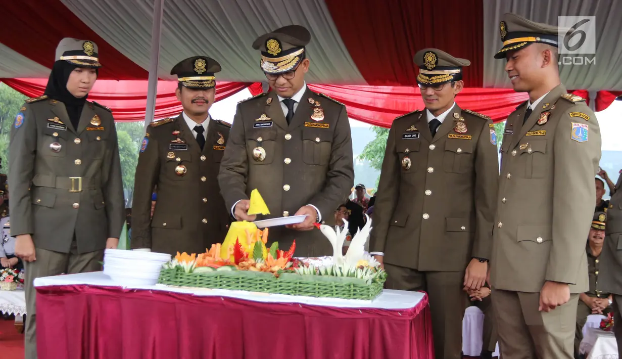 Gubernur DKI Anies Baswedan didampingi Wakil Gubernur, Sandiaga Uno memotong tumpeng dalam peringatan HUT Satpol PP ke-68 di Monas, Jakarta, Kamis (26/4). Tumpeng itu diberikan kepada Satpol PP termuda dan anggota tertua. (Liputan6.com/Arya Manggala)