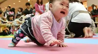 Seorang bayi menangis dan ingin menghampiri ibunya saat kompetisi 'Bayi Merangkak',  Yokohama, Jepang, Senin (23/11/2015). Tingkah bayi yang lucu menjadi pemandangan yang menggemaskan bagi para penonton. (AFP Photo/Kazuhiro Nogi)