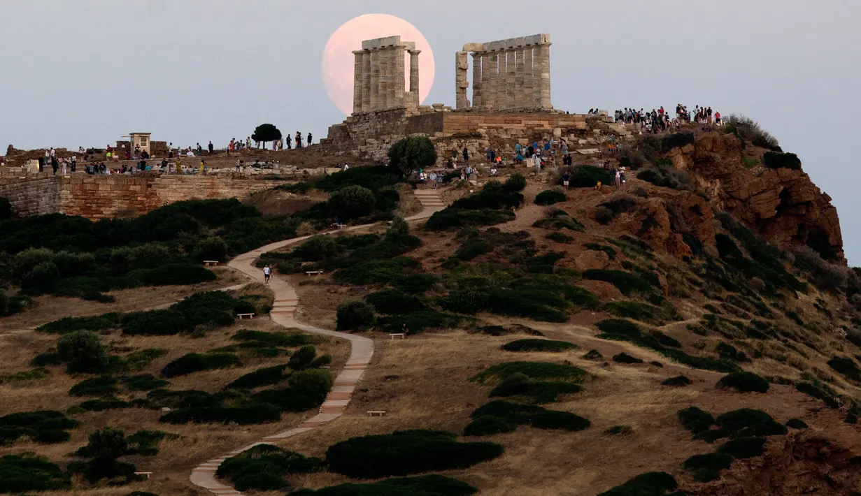 Pengunjung menyaksikan pemandangan bulan purnama hampir penuh yang menampakkan diri di langit Kuil Poseidon kuno di Cape Sounion, sekitar 70 kilometer sebelah tenggara Athena, Yunani (2/8/2020). (Xinhua/Marios Lolos)