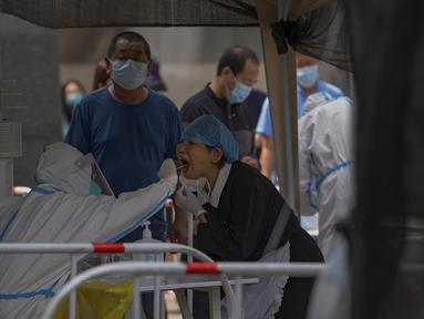 Warga diambil sampel lendir tenggorokan di tempat pengujian COVID-19 di distrik Chaoyang di Beijing, Selasa (14/6/2022). Pihak berwenang memerintahkan pengujian massal tiga hari di antara sekitar 3,5 juta penduduknya menyusul terdeteksinya ratusan kasus virus corona COVID-19 terkait dengan klaster bar 24 jam. (AP Photo/Andy Wong)