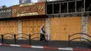Seorang pria berjalan melewati toko-toko yang tutup di sepanjang jalan di kota Hebron di Tepi Barat yang diduduki saat terjadi pemogokan umum yang diserukan sebagai tanggapan atas serangan ke kompleks rumah sakit di Gaza, Rabu (18/10/2023). (HAZEM BADER / AFP)