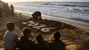Cuaca ekstrem yang ditandai dengan hujan deras, angin kencang, dan suhu dingin memperburuk kondisi pengungsi Palestina di Gaza hingga menimbulkan angka kematian baru. Tampak dalam foto, anak-anak menyaksikan seniman Yazed Abo Jarad membuat patung pasir untuk tahun mendatang di Deir El-Balah, Jalur Gaza tengah pada 30 Desember 2025. (Bashar Taleb/AFP)