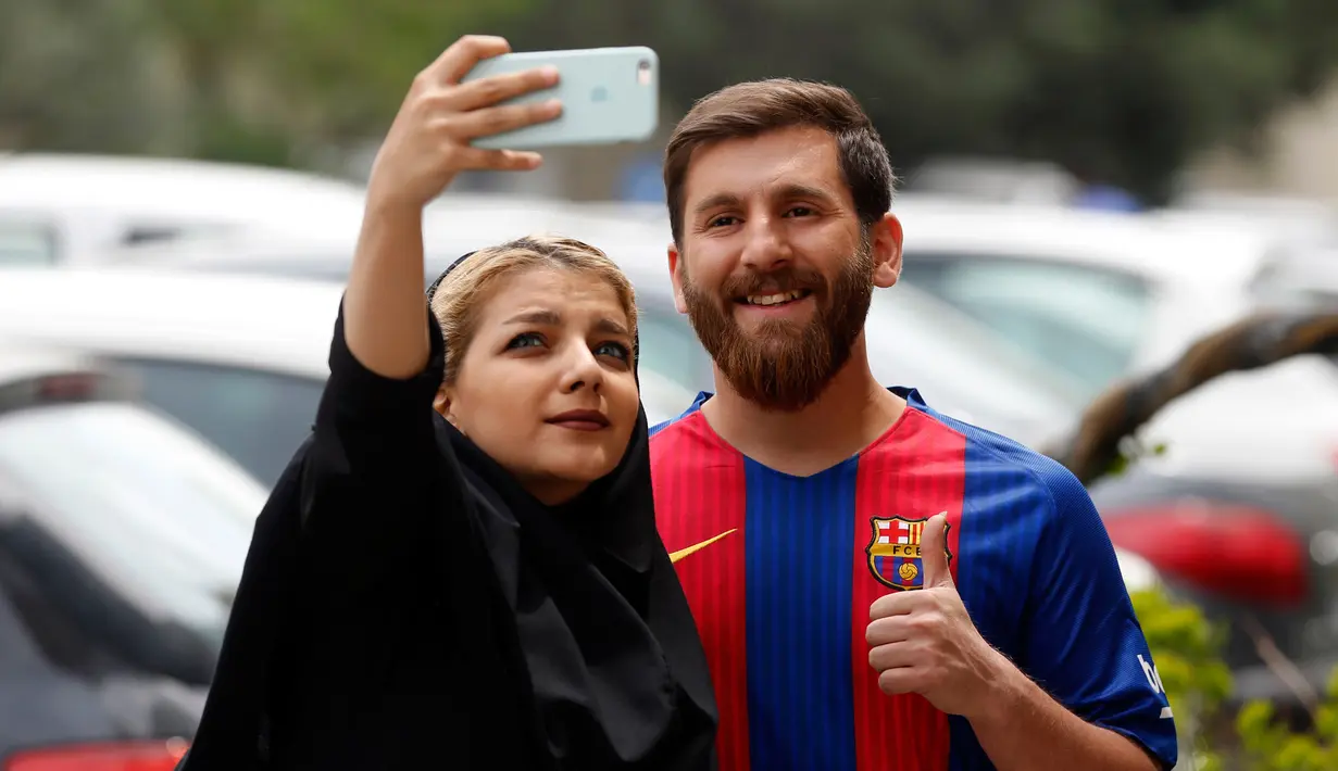 Pemuda asal Iran, Reza Parastesh berswafoto dengan seorang penggemar di sebuah jalan di Teheran, Senin (8/5). Reza Parastesh harus dibawa ke kantor polisi akhir pekan lalu gara-gara terlalu mirip dengan bintang Barcelona, Lionel Messi. (ATTA KENARE/AFP)