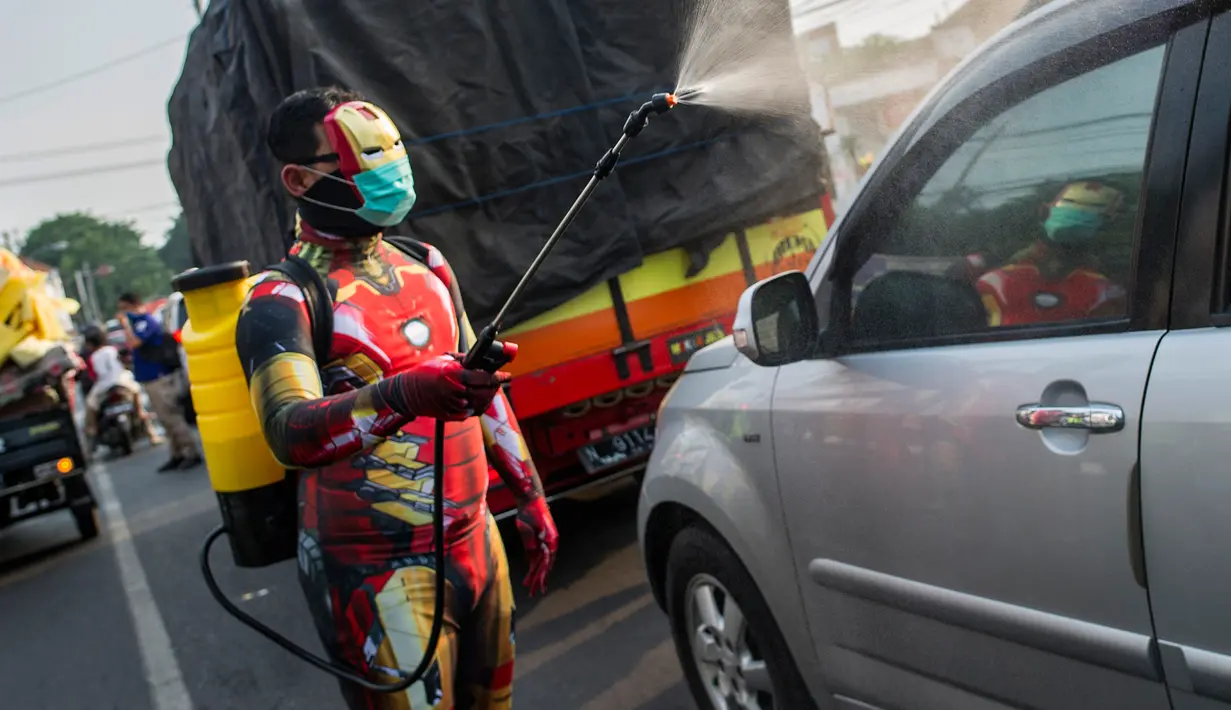 Petugas kepolisian yang berpakaian superhero menyemprotkan cairan disinfektan di jalan kawasan Pasuruan, Jawa Timur, Kamis (9/4/2020). Penyemprotan cairan disinfektan tersebut bertujuan untuk mengantisipasi penyebaran Virus Corona (COVID-19). (JUNI KRISWANTO / AFP)