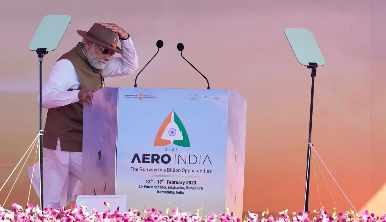 Perdana Menteri India Narendra Modi memegang topinya saat dia berjalan untuk memberikan pidato kepada para delegasi saat peresmian Aero India 2023 di pangkalan udara Yelahanka, Bengaluru, India, Senin (13/2/2023). Aero India adalah acara dua tahunan dengan demonstrasi terbang oleh tim pengganti dan militer serta paviliun komersial tempat perusahaan penerbangan memamerkan produk dan teknologi mereka. (AP Photo/Aijaz Rahi)
