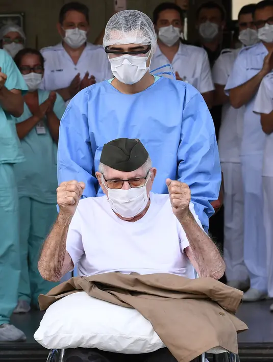 Veteran Perang Dunia II asal Brasil, Ermando Armelino Piveta meninggalkan Rumah Sakit Angkatan Bersenjata setelah pulih dari covid-19 di Brasilia, Selasa (14/4/2020). Kakek 99 tahun itu dipulangkan dari rumah sakit diiringi penghormatan militer dengan terompet dan tepuk tangan. (EVARISTO SA/AFP)
