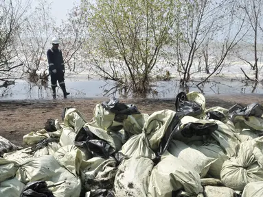 Pegawai Pertamina melintas di depan tumpukkan karung berisi limbah tumpahan minyak (oil spill) di Pantai Muara Beting, Muara Gembong, Bekasi, Jawa Barat, Minggu (28/7/2019). Oil spill akibat kebocoran terjadi di sumur lepas pantai YYA1 Karawang. (merdeka.com/Iqbal S. Nugroho)