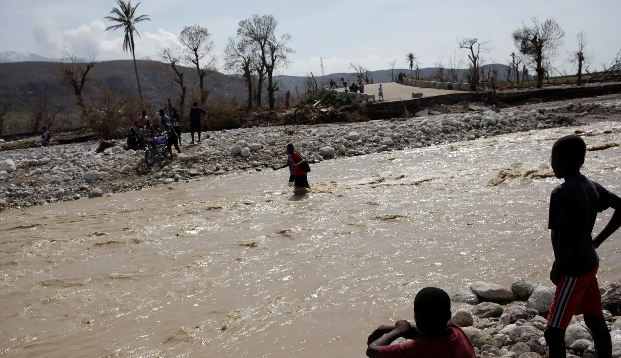 Dua bocah mengamati warga yang berusaha menyeberangi sungai beraliran deras di Les Anglais, 10 Oktober 2016. Selain merusak ribuan rumah, badai Matthew di Haiti juga memutus jembatan yang merupakan akses utama warga. (REUTERS/Andres Martinez Casares)