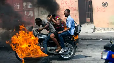 Pengendara sepeda motor melewati barikade ban yang terbakar saat terjadi protes krisis bahan bakar di Port-au-Prince, Haiti, Senin (16/9/2019). Krisis bahan bakar menyebabkan transportasi umum tidak beroperasi. (AP Photo/Dieu Nalio Chery)