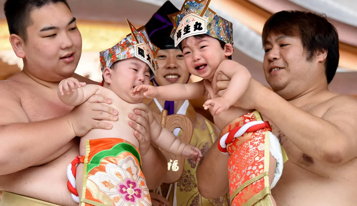 Dua pesumo menggendong bayi yang menangis selama Festival Nakizumo atau kontes bayi menangis di kuil Kamegaike-Hachiman, Jepang, Minggu (14/5). Festival lebih dari 400 tahun ini sudah berlangsung turun-temurun dari leluhur. (Toru YAMANAKA/AFP)