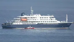 Tertahannya Kapal pesiar MV Hondius di lepas pantai Praia, Tanjung Verde, menyusul wabah mematikan Hantavirus yang terjadi. Tampak dalam foto, sebuah perahu ambulans yang membawa awak kapal yang mengenakan pakaian pelindung bahan berbahaya (hazmat suit) mendekati pintu kemudi di sisi kanan kapal pesiar MV Hondius, saat kapal tersebut berhenti di lepas pelabuhan Praia, ibu kota Tanjung Verde, pada Selasa 5 Mei 2026. (Foto oleh AFP)