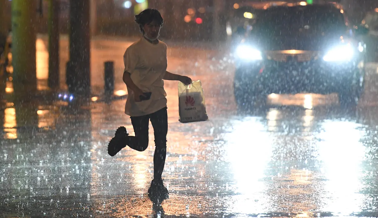Seorang wanita berlari di bawah guyuran hujan di Distrik Chaoyang, Beijing, China (12/8/2020). Badan meteorologi Beijing mengeluarkan peringatan siaga kuning untuk hujan badai. (Xinhua/Ju Huanzong)