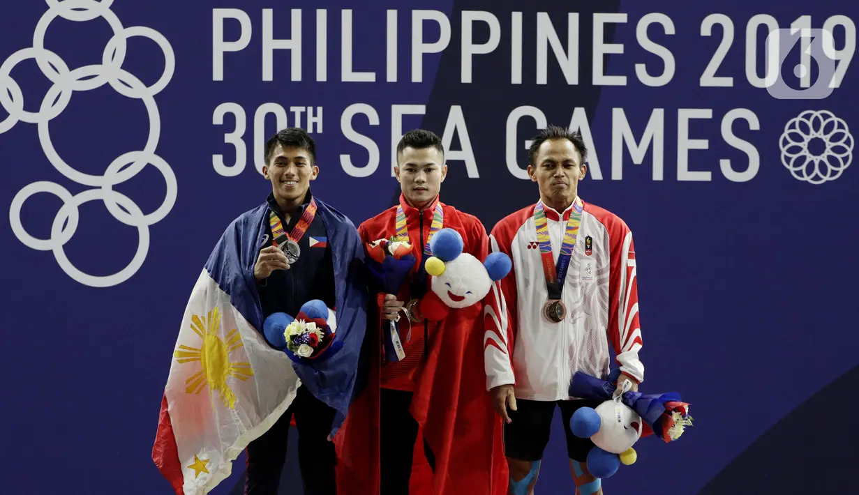 Lifter putra Indonesia, Suratman (kanan) saat naik podium usai mendapatkan medali perunggu SEA Games 2019 cabang angkat besi nomor 55 kg di Stadion Rizal Memorial, Manila, Minggu (1/12/2019). Dirinya meraih perak dengan total angkatan 250 kg. (Bola.com/M Iqbal Ichsan)