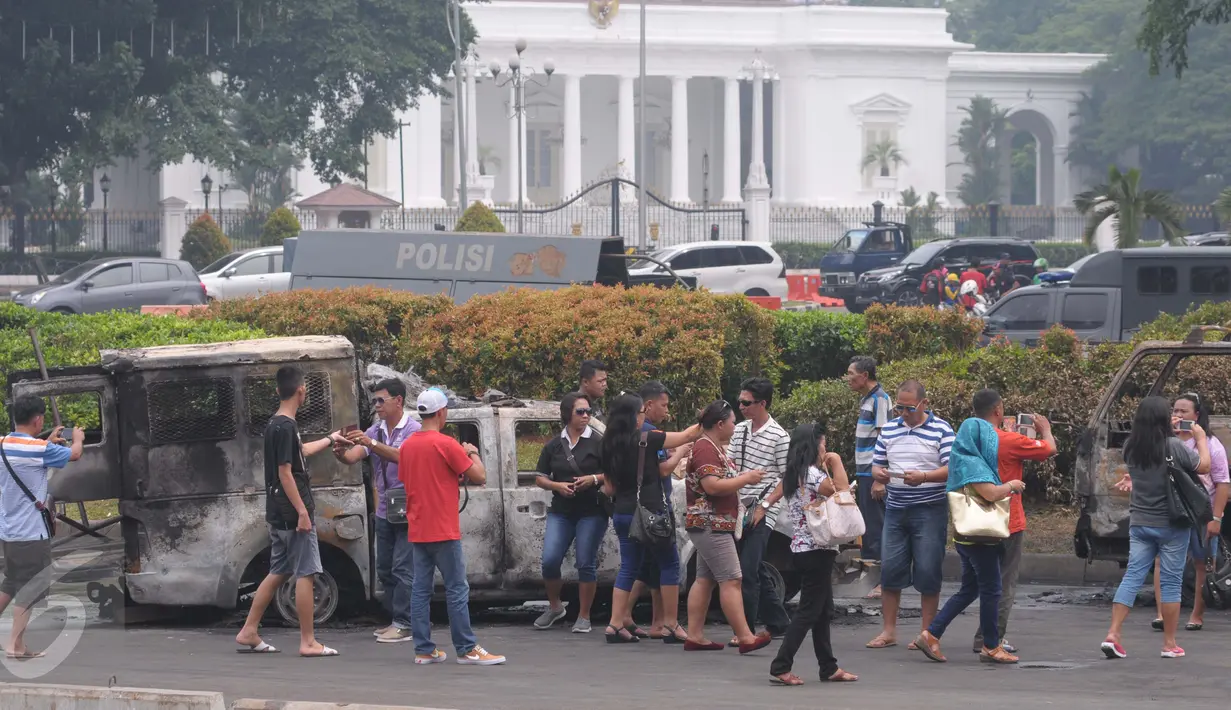 Sejumlah warga melihat mobil aparat yang dibakar demonstran 4 November di kawasan Monas, Jakarta, Sabtu (5/11). Pengunjung menjadikan dua kendaraan milik kepolisian tersebut sebagai objek foto dan melakukan swafoto. (Liputan6.com/Angga Yuniar)