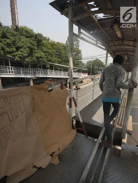 Pejalan kaki melewati lubang di atas JPO di Halte Bus Transjakarta di Jembatan Gantung, Cengkareng, Jakarta, Jumat (27/7). JPO yang rusak akibat tertabrak truk sejak setahun lalu hingga kini belum diperbaiki.  (Liputan6.com/Arya Manggala)