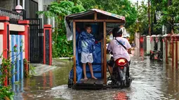 Ketinggian air bervariasi, dan di beberapa lokasi, warga terpaksa harus menembus banjir dengan sepeda motor mereka. Tampak dalam foto, seorang pria bersama seorang anak melewati banjir di jalan yang tergenang setelah hujan deras di permukiman Darul Imarah, pinggiran Banda Aceh, pada Kamis 27 November 2025. (CHAIDEER MAHYUDDIN/AFP)