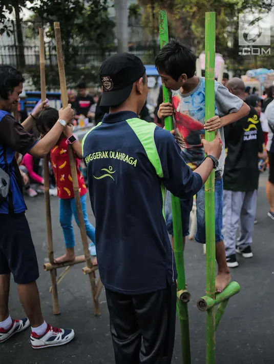 Anak-anak bermain permainan tradisional egrang ditemani sejumlah mahasiswa dari Penggerak Olahraga saat car free day (CFD) di kawasan Bundaran HI, Jakarta, Minggu (14/7/2019). Kegiatan yang rutin digelar ini bertujuan mengajak masyarakat DKI Jakarta aktif berolahraga. (Liputan6.com/Faizal Fanani)