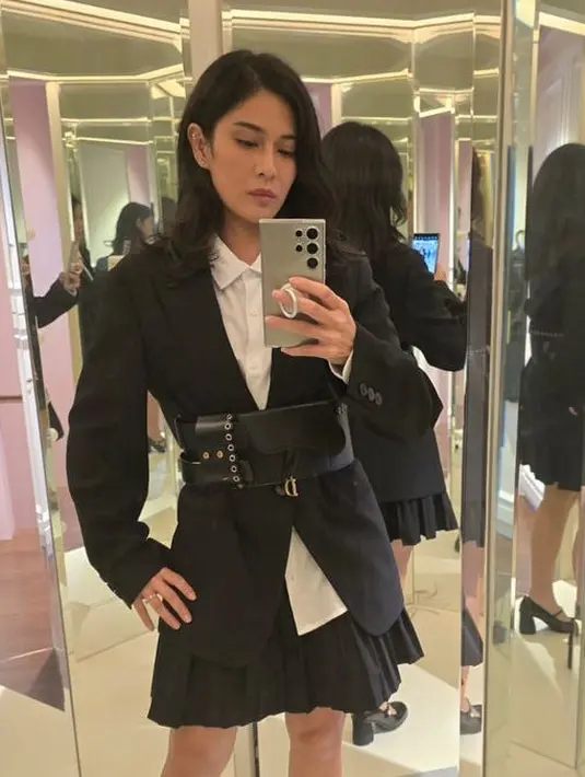 Dian Sastrowardoyo mengenakan blazer hitam oversize dipadukan inner kemeja putih dan mini skirt pleated. Serta belt hitam besar yang menjadi statement. [@therealdisastr]