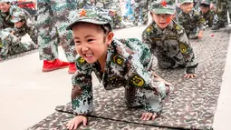 Sejumlah anak-anak berbaris sambil merangkak saat mensimulasikan latihan militer di sebuah taman kanak-kanak di provinsi Henan, China (30/5). (AFP)