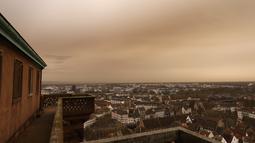 Pemandangan kota Strasbourg tampak diselimuti debu Sahara berwarna oranye bergerak di atas kota di Prancis timur (15/3/2022). Badai di gurun Sahara menciptakan badai besar hembusan angin, yang mengangkat pasir ke udara. (AP Photo/Jean-Francois Badias)