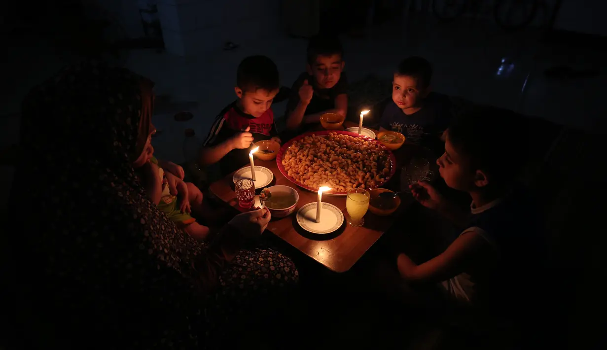 Sebuah keluarga Palestina menikmati makan sahur selama pemadaman listrik di kamp pengungsian Rafah, Jalur Gaza selatan, 11 Juni 2017. Israel mengumumkan pihaknya mengurangi pasokan listriknya ke Gaza atas permintaan Otoritas Palestina. (SAID KHATIB/AFP)