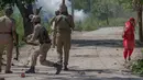 Seorang wanita berjalan disamping polisi India saat bentrokan di Srinagar, Kashmir yang dikuasai India, (23/5). Bentrokan telah meningkat setelah tentara menggerebek sebuah perguruan tinggi di kota selatan Pulwama bulan lalu. (AP Photo/Dar Yasin)