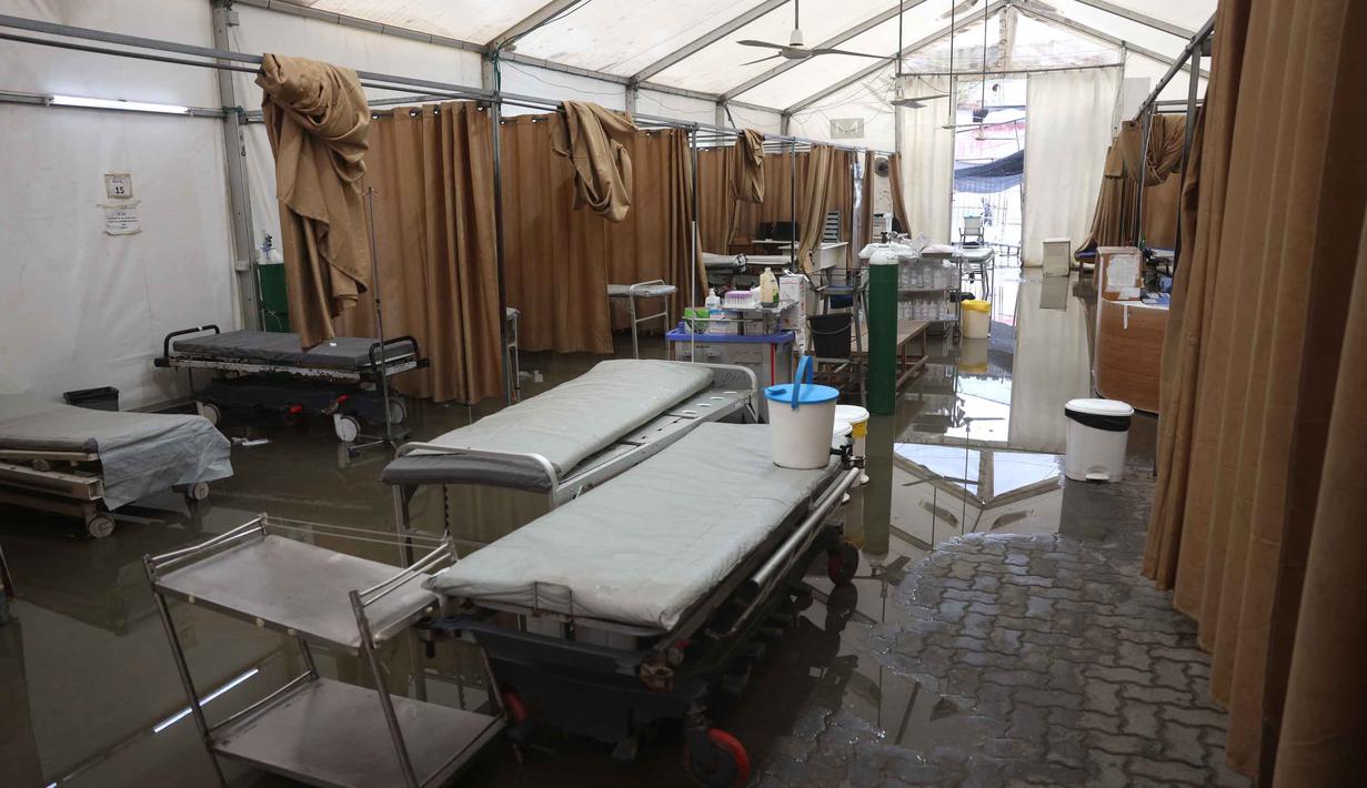 Imbasnya, layanan Instalasi Gawat Darurat (IGD) di tenda tersebut ditutup sementara. Tampak dalam foto, ranjang-ranjang kosong di dalam tenda darurat milik Rumah Sakit Nasser, yang berfungsi sebagai tempat penerimaan pasien rawat jalan dan departemen gawat darurat, setelah hujan lebat di Khan Yunis di Jalur Gaza selatan pada 26 Maret 2026. (Bashar Taleb/AFP)