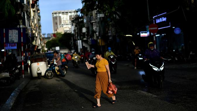 Seorang perempuan menyeberang jalan sebelum hujan lebat mengguyur Hanoi, ibu kota Vietnam pada 11 Agustus 2020. Setelah mencatat nol kasus COVID-19 selama lebih dari tiga bulan, Vietnam melaporkan sejumlah infeksi baru di dalam negeri sejak akhir Juli. (MANAN VATSYAYANA/AFP)