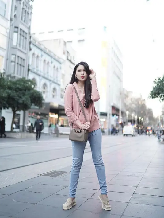 <p>Selain itu, perempuan 39 tahun ini juga membagikan deretan foto OOTD-nya dengan outfit kasual yang chic dan stylish. Seperti potret ini, ia tampak memadupadankan kardigan pink dengan skinny jeans warna biru muda, sepatu slip on warna ash grey, dan sling bag warna senada. (Instagram/sandradewi88).</p>